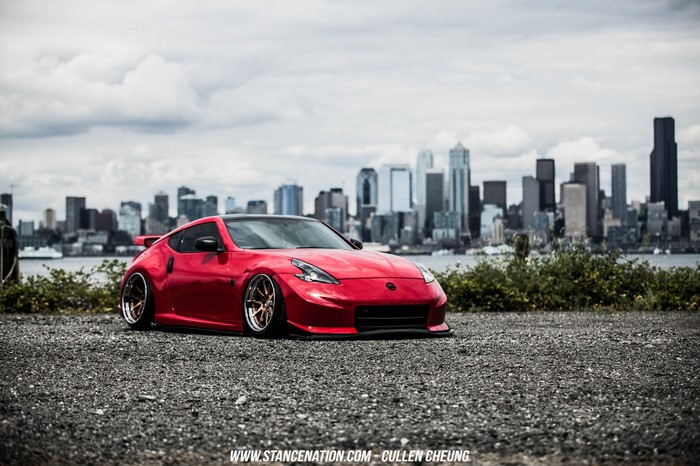Red Nissan 370Z on gravel with city skyline