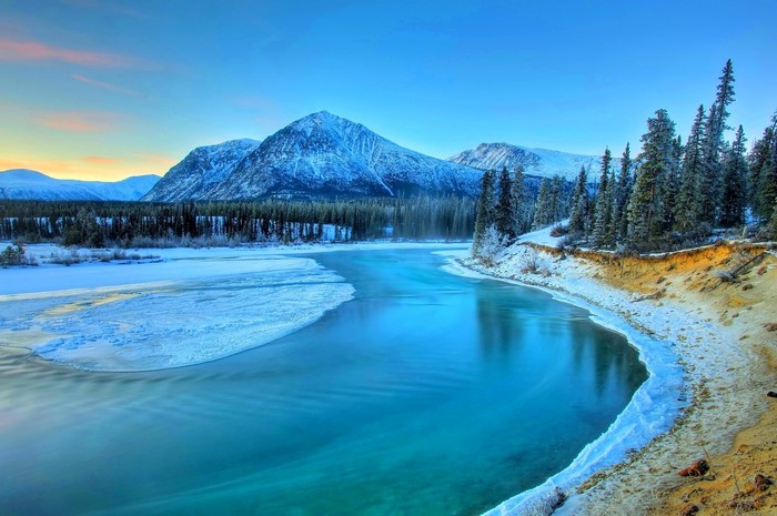 River flowing through a snowy landscape with mountains and forest