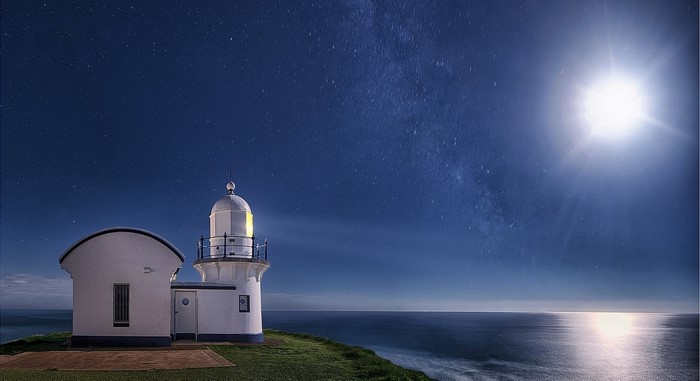 Lighthouse under a starry night sky with moon