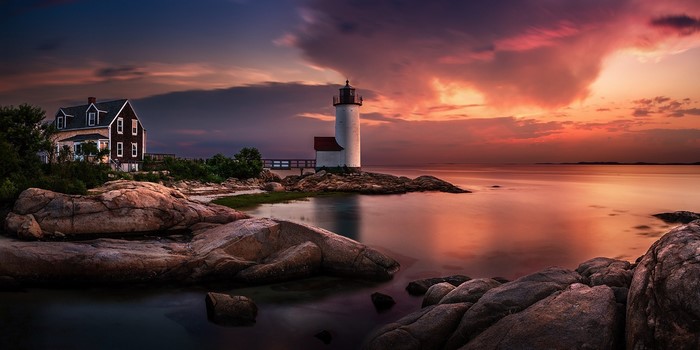 Sunset over the ocean with a lighthouse and house