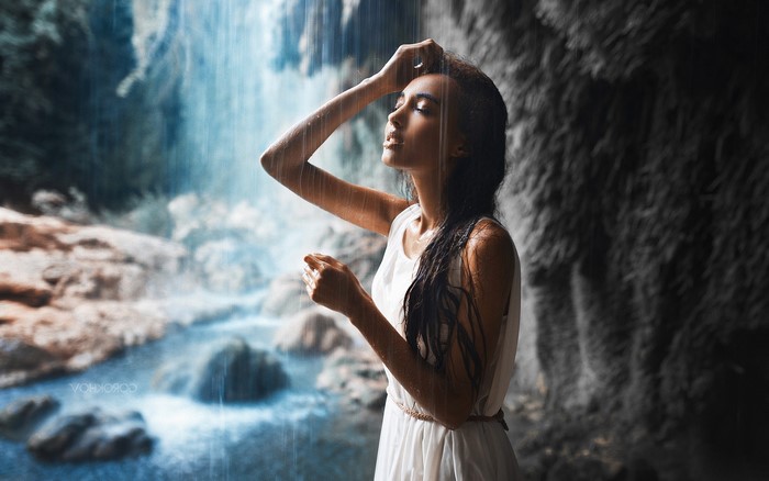 Woman in white dress standing in the rain near a waterfall