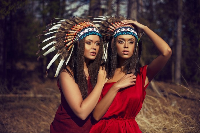 Two women in Native American headdresses in a forest