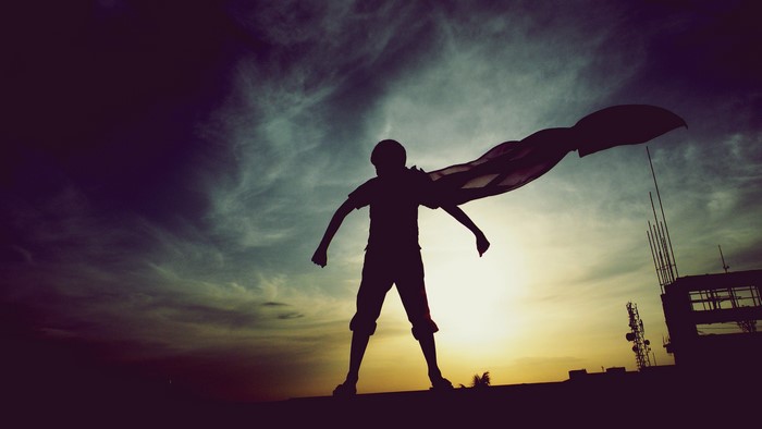 Silhouette of a child with a cape against the sunset
