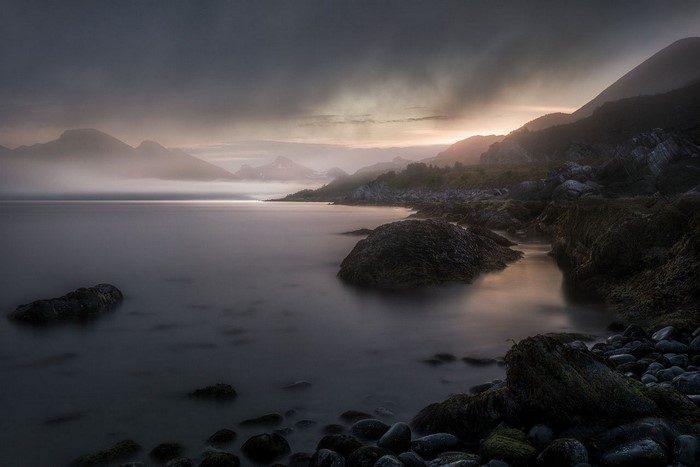 Misty mountains and rocky coast at sunset