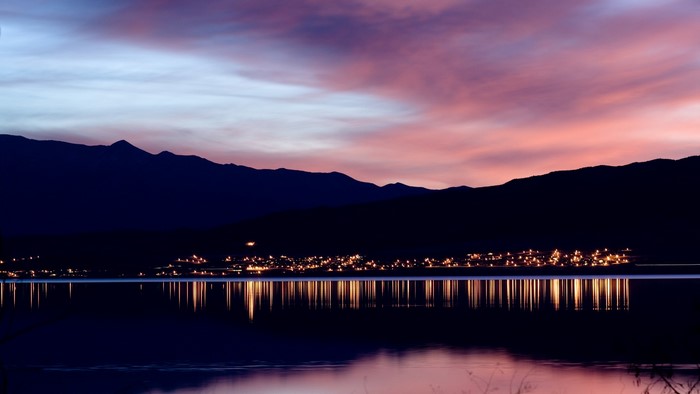 City lights reflected on a calm lake at sunset with mountains