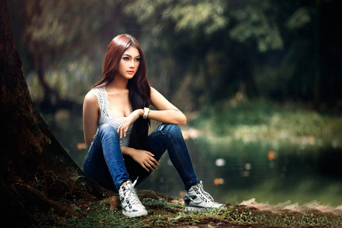 Asian woman with long hair sitting by a tree