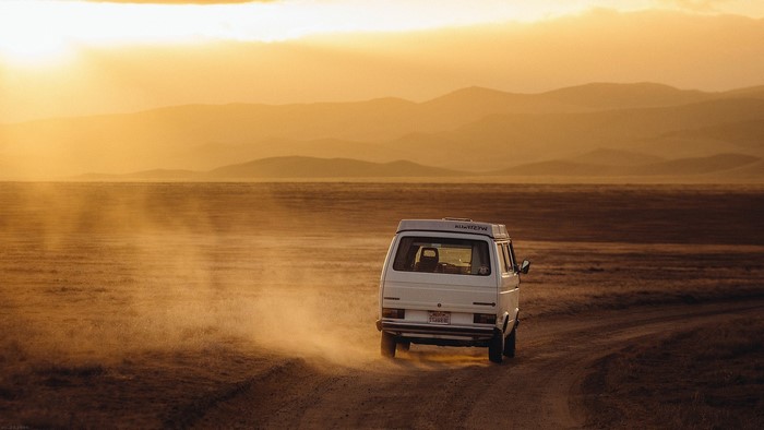White van driving on a dirt road at sunset