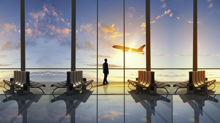 Man watches airplane take off from airport lounge at sunset