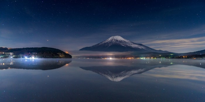 Mount Fuji reflected in a lake at night under a starry sky