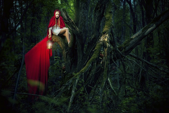 Woman in red hood with lantern in forest