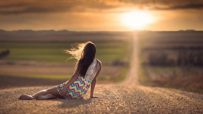 Woman sitting on a road at sunset
