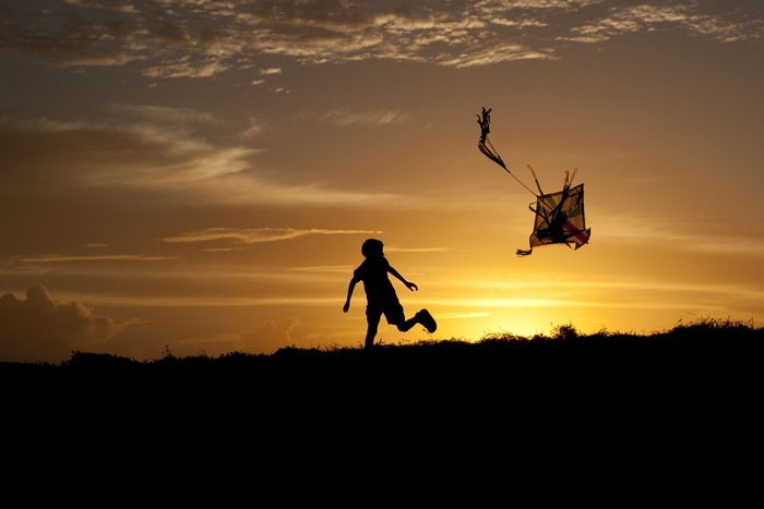 Silhouette of a child flying a kite at sunset