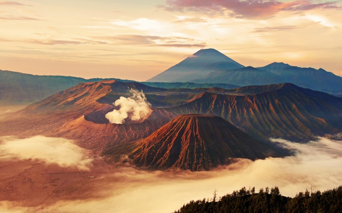 Volcanoes erupting with smoke at sunrise over clouds