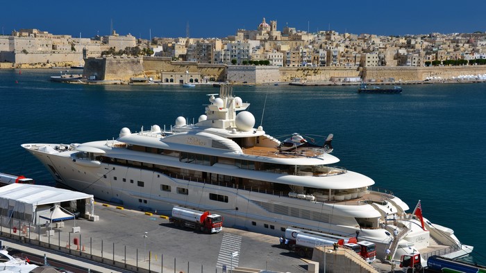 Superyacht Dilbar docked in a harbor with city in background