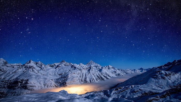 Snowy mountains under a starry sky with mist