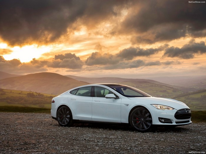 White Tesla Model S parked on gravel with dramatic sunset sky