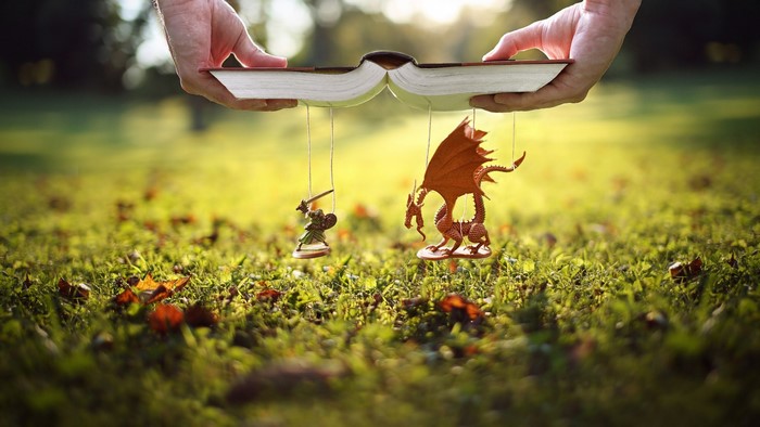 Hands holding book with knight and dragon miniatures