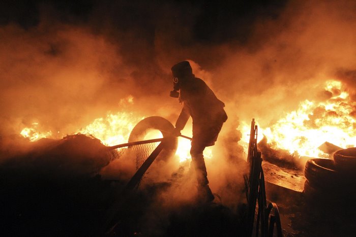 Protestor with gas mask in front of fire in Kyiv