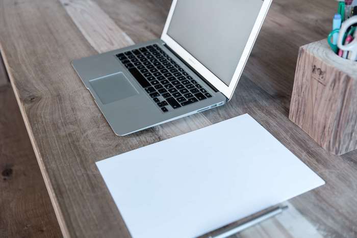 MacBook on a wooden table with paper and pen