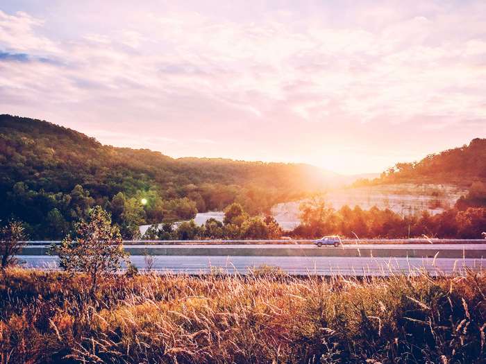 Car on highway at sunset with hills and trees