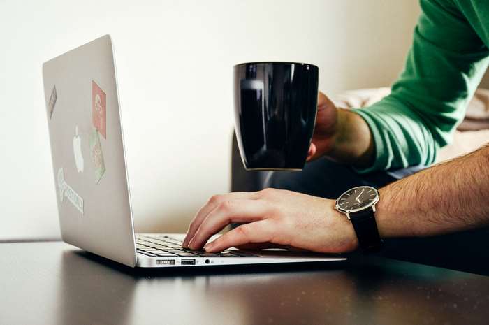 Man with coffee mug using Apple MacBook laptop