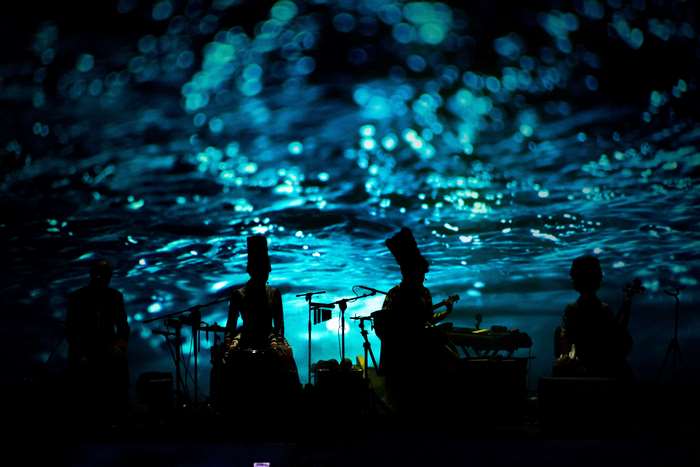 Musicians performing on a stage with a water-like projection