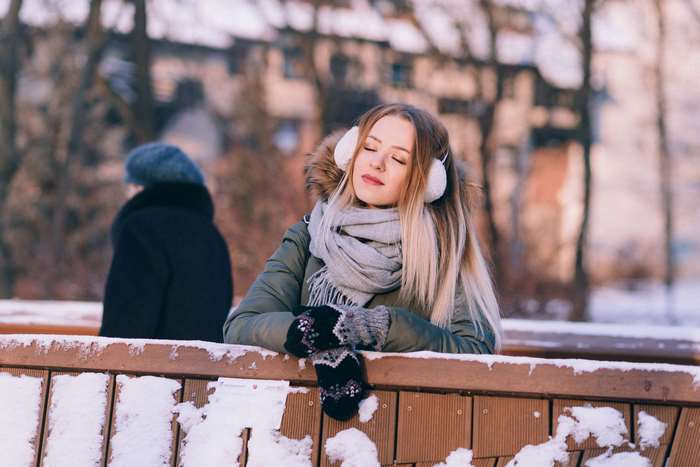Young woman wearing earmuffs and scarf in winter park 4K