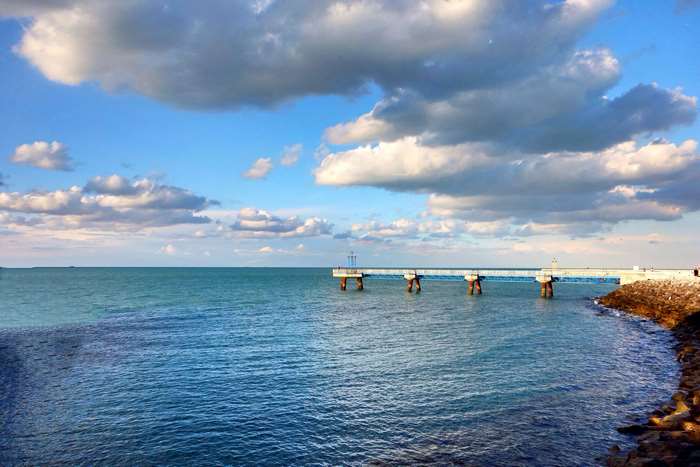 Pier over the sea with clouds and rocky shore