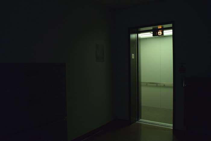 Open elevator with glowing arrow sign in dark hallway