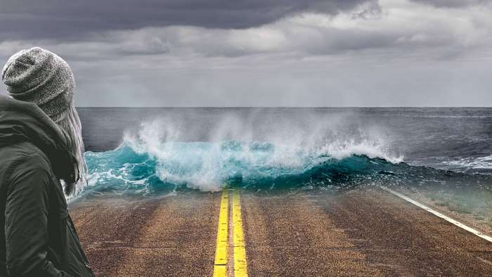 Person watching a wave crash on a flooded road