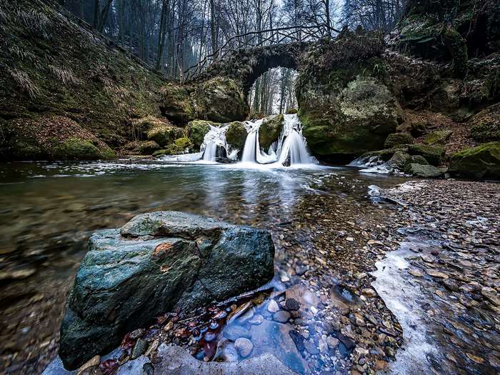 Waterfall flowing under a wooden bridge in a forest