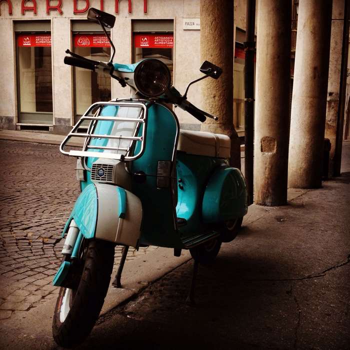 Turquoise and white Vespa scooter parked on cobblestone street