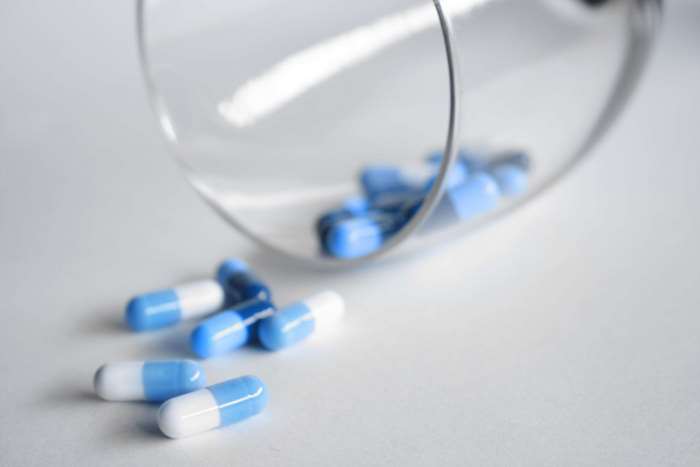 Blue and white capsules spilling from a glass 4K