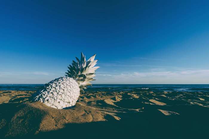 White pineapple on a sandy beach with ocean and blue sky