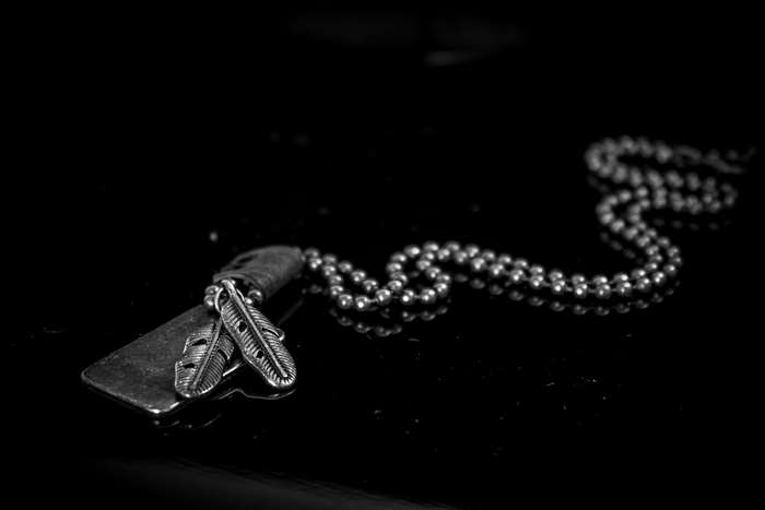 Necklace with dog tag pendant and feather charms on black background