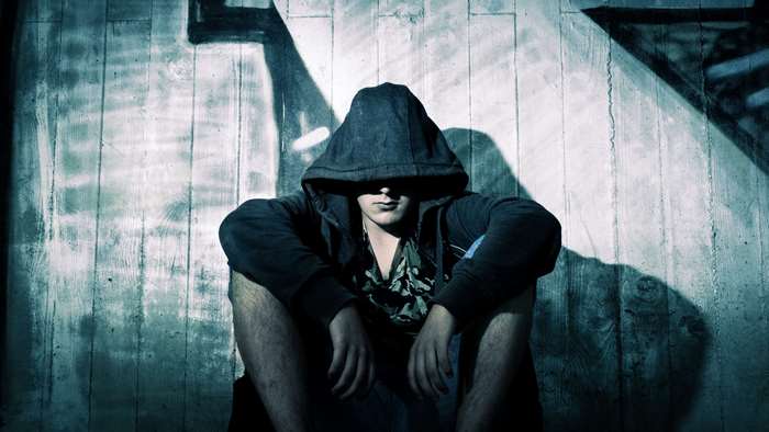 Man in hoodie sitting in front of wooden wall with shadows