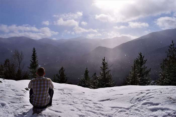 Man sitting on snowy mountain top with sunlit clouds