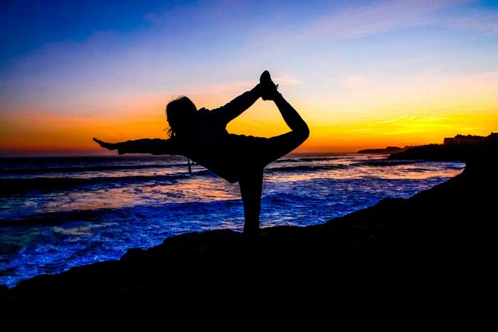 Woman practicing yoga on a beach at sunset