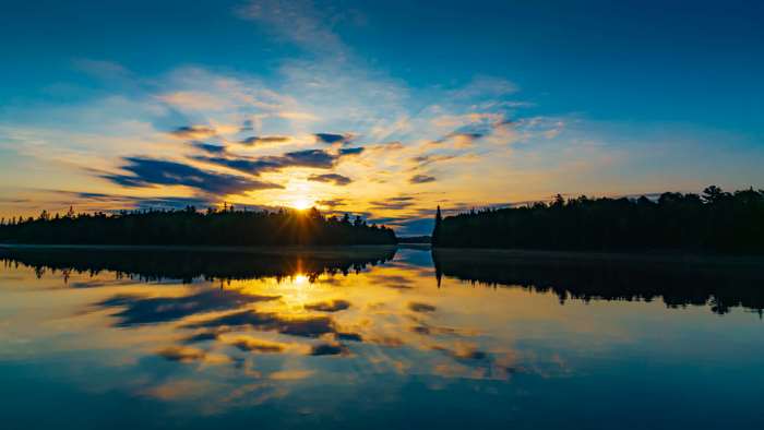 Sunrise over a tranquil lake with forest reflections