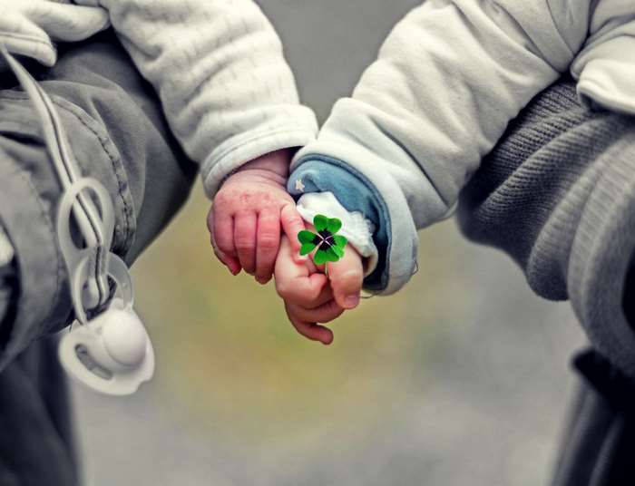 Two babies holding hands with a four-leaf clover