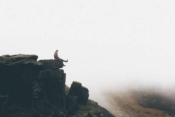 Person sitting on a rocky cliff edge in fog