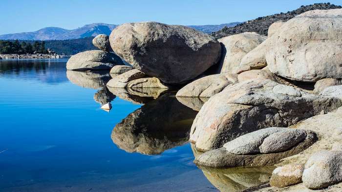 Large boulders on the shore of a calm lake with mountains in the background