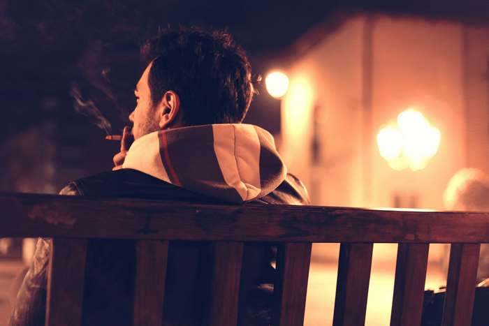 Man smoking a cigarette on a bench at night