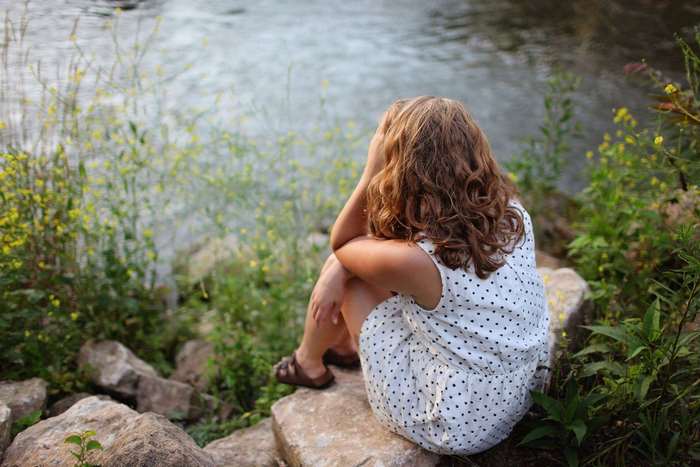 Woman sitting by a river with her head in her hands