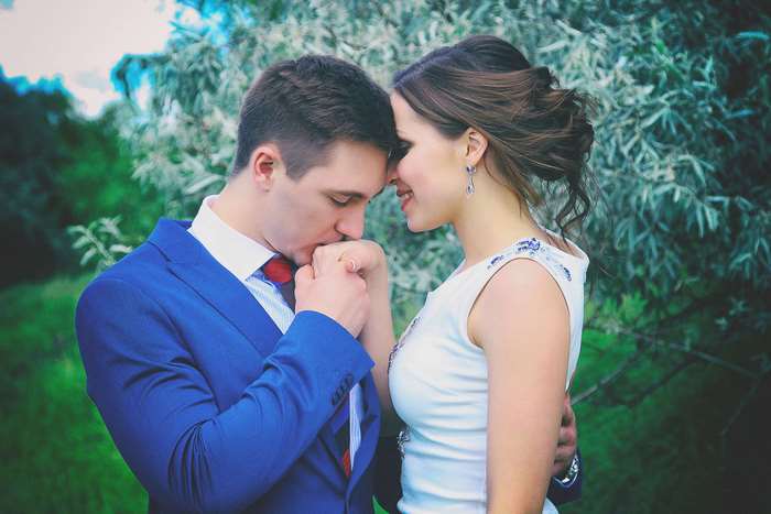 Groom kissing bride's hand in designer suit outdoors