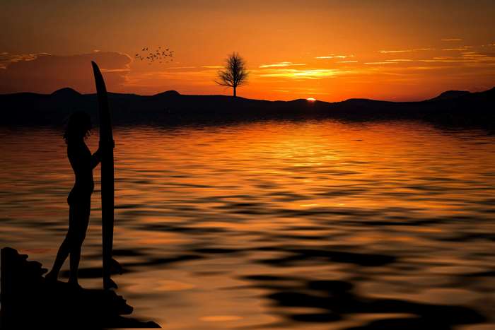 Silhouette of a woman with a surfboard at sunset