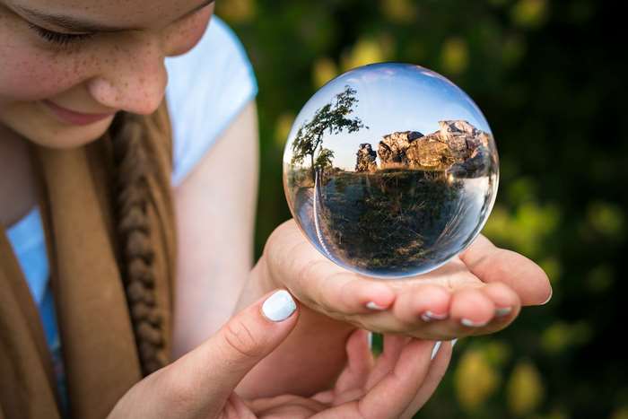 Girl holding a glass ball with landscape reflection