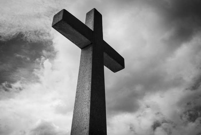 Black and white low angle shot of a cross against cloudy sky