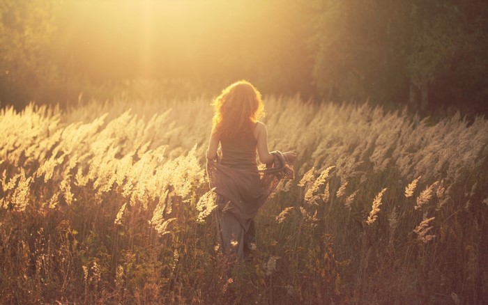 Girl walking through a field of grass at sunset