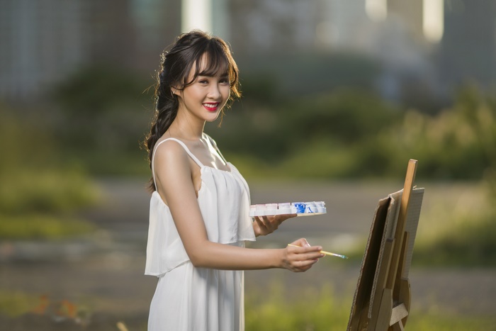 Young Woman Painting Outdoors in White Dress